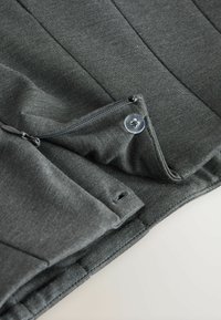 Sivi materijal s glatkom teksturom ima džep s patentnim zatvaračem i detalj s dugmetom, pokazujući čiste linije i čvrsto šivanje.