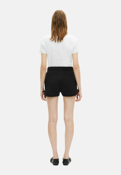 Zwarte shorts met een gladde textuur, voorzien van een ontspannen pasvorm en een elastische tailleband. Gecombineerd met een eenvoudig wit T-shirt.