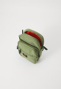 Borsa in tessuto verde con due compartimenti con zip, internamente arancione, con hardware nero e un'etichetta sul fronte.