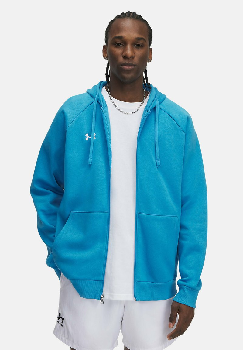 Blaues Zip-Hoodie aus weichem Stoff, mit einer Kordelzugkapuze, Fronttaschen und einem gestickten Logo auf der Brust. Darunter ein schlichtes weißes T-Shirt.