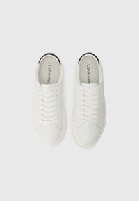 Sneakers albe din piele cu șireturi plate, vârf rotund și un accent texturat negru la călcâi. Logo-ul este imprimat pe branț. Design casual.