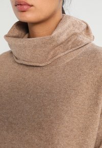 Kaneelkleurige turtleneck trui van zacht, textuurgebreid materiaal, met een omgeslagen kraag en een licht ontspannen pasvorm.