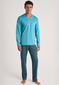 Heren pyjama set met een turquoise lange mouw V-hals shirt met een zak en patroon navy broeken met witte accenten. Zachte stof.