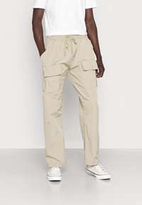 Béžové cargo kalhoty s volným střihem, páskem na šňůrku a několika bočními kapsami. Vyrobené z lehké látky, vhodné pro volnočasové nošení.