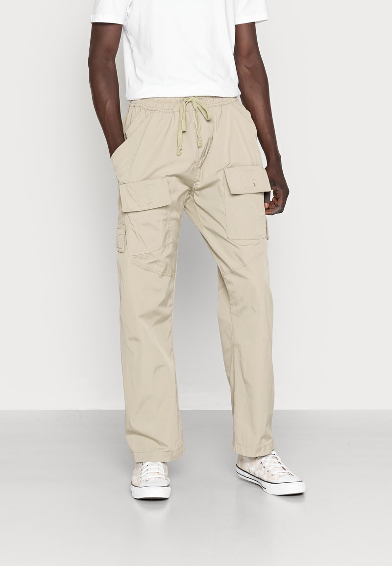 Béžové cargo kalhoty s volným střihem, páskem na šňůrku a několika bočními kapsami. Vyrobené z lehké látky, vhodné pro volnočasové nošení.