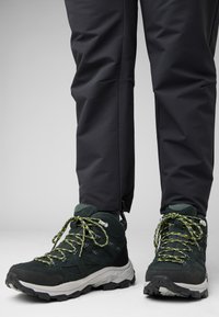 Stivali da trekking verdi con tessuto texturizzato, accenti neri e lacci giallo brillante. Indossati con pantaloni flessibili scuri, con una vestibilità slim.