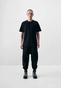 Black short-sleeve t-shirt and black cargo pants made of a soft, textured fabric. Footwear features a gray and black design with distinctive accents.