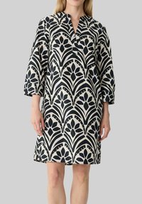 Schwarz-creamfarbenes, gemustertes Kleid mit V-Ausschnitt und Dreiviertelärmeln, das ein florales geometrisches Design aus einem glatten Stoff präsentiert.
