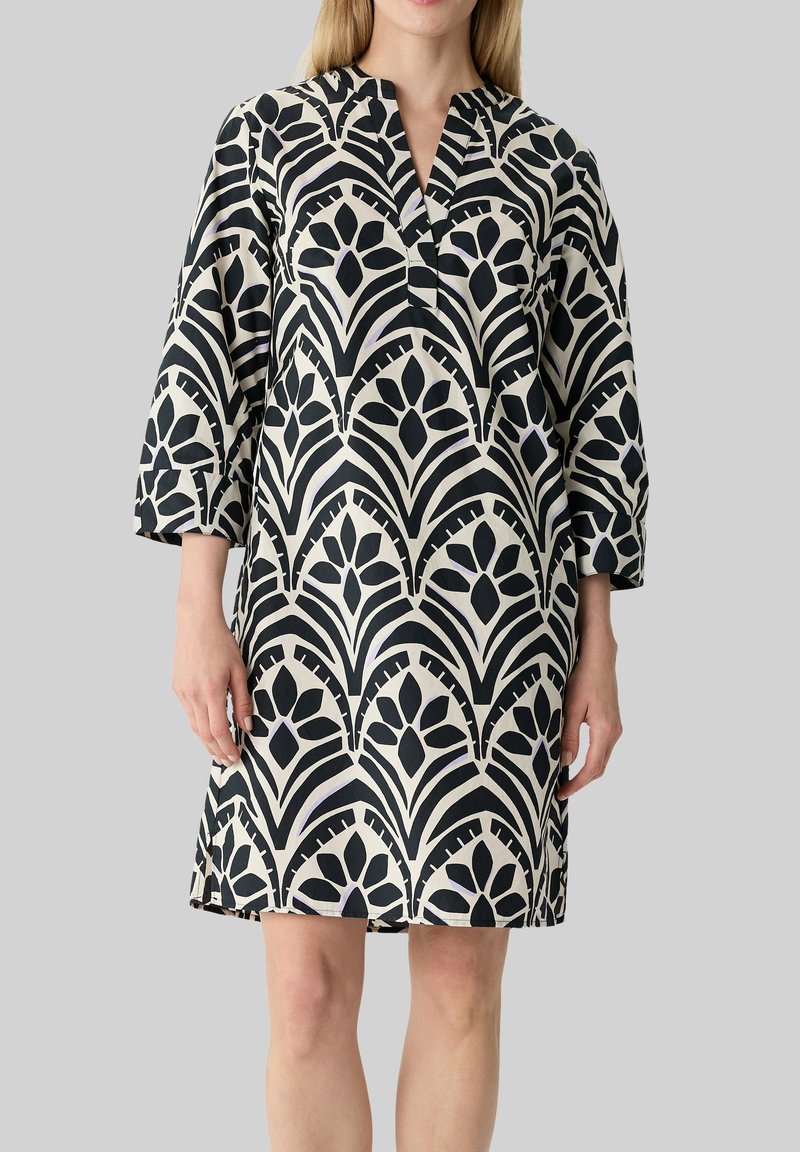 Schwarz-creamfarbenes, gemustertes Kleid mit V-Ausschnitt und Dreiviertelärmeln, das ein florales geometrisches Design aus einem glatten Stoff präsentiert.
