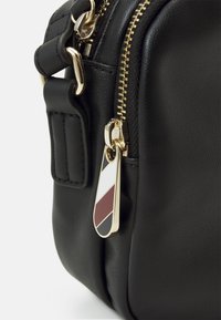 Borsa in pelle nera con zip e accessori dorati. Include un'etichetta con strisce diagonali rosse, bianche e nere. Finitura testurizzata.