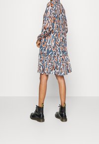 Tiskované šaty s modrým, oranžovým a šedým vzorem. Mají dlouhé rukávy a tiered volánkový lem. Nosené s černými šněrovacími kotníkovými botami.