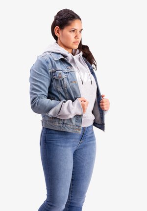 Denim jacket with a slightly fitted cut, light blue color, and classic design. Worn over a gray sweatshirt with a hood.