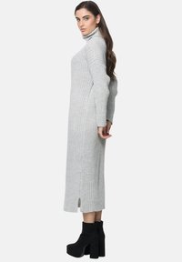 Graues geripptes Rollkragenkleid mit langen Ärmeln, seitlichen Schlitzen und figurbetonter Silhouette, kombiniert mit hohen schwarzen Stiefeln mit breitem Absatz.