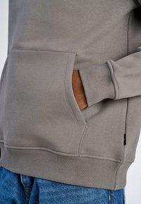 Grijze sweatshirt met een kangoeroezak, ribgebreide manchetten en zoom, gemaakt van textuurstof, gedragen met blauwe denim jeans.