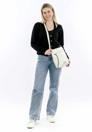 Borsa a spalla bianca con chiusura a zip, rifiniture nere a contrasto e tracolla regolabile. Il cardigan nero e i jeans azzurri completano il look.