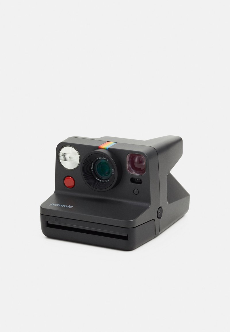 Instant camera with a matte black body, a round lens, a flash, red button, and a colorful stripe on top. Compact design with film slot at front.