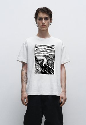 Hvid bomulds t-shirt med et sort grafisk print af en figur på en bro med svungne linjer og minimale baggrundsdetaljer.