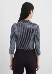 Navy-blaues Langarmbluse mit einem weißen geometrischen Muster, mit hohem Kragen und tailliertem Design, kombiniert mit maßgeschneiderten schwarzen Hosen.