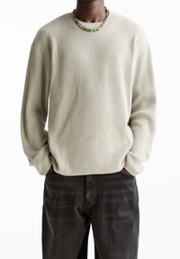 Hellgrüner, gerippter Pullover mit lockerem Schnitt, rundem Ausschnitt und langen Ärmeln. Kombiniert mit dunkelgrauen Jeans und einer Perlenkette.