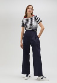 Navy wide-leg trousers paired with a striped short-sleeve shirt featuring red accents. The model wears white sneakers. Minimalistic background.