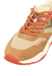 Brown suede and mesh sneaker with orange laces, green accents, and red rubber outsole. Features textured detailing and a cushioned sole.