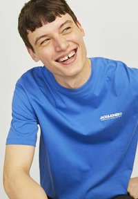 Mėlynas medvilninis marškinėliai su apvaliu iškirpimu ir trumpomis rankovėmis. Ant krūtinės yra baltas logotipas. Lygi tekstūra, kasdieniškas siluetas.