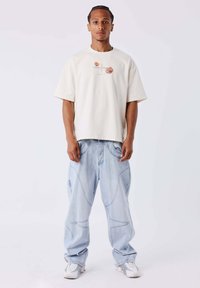 Camiseta de manga corta beige con bordado floral, combinada con unos vaqueros oversized de color azul claro con costuras únicas y bolsillos laterales.