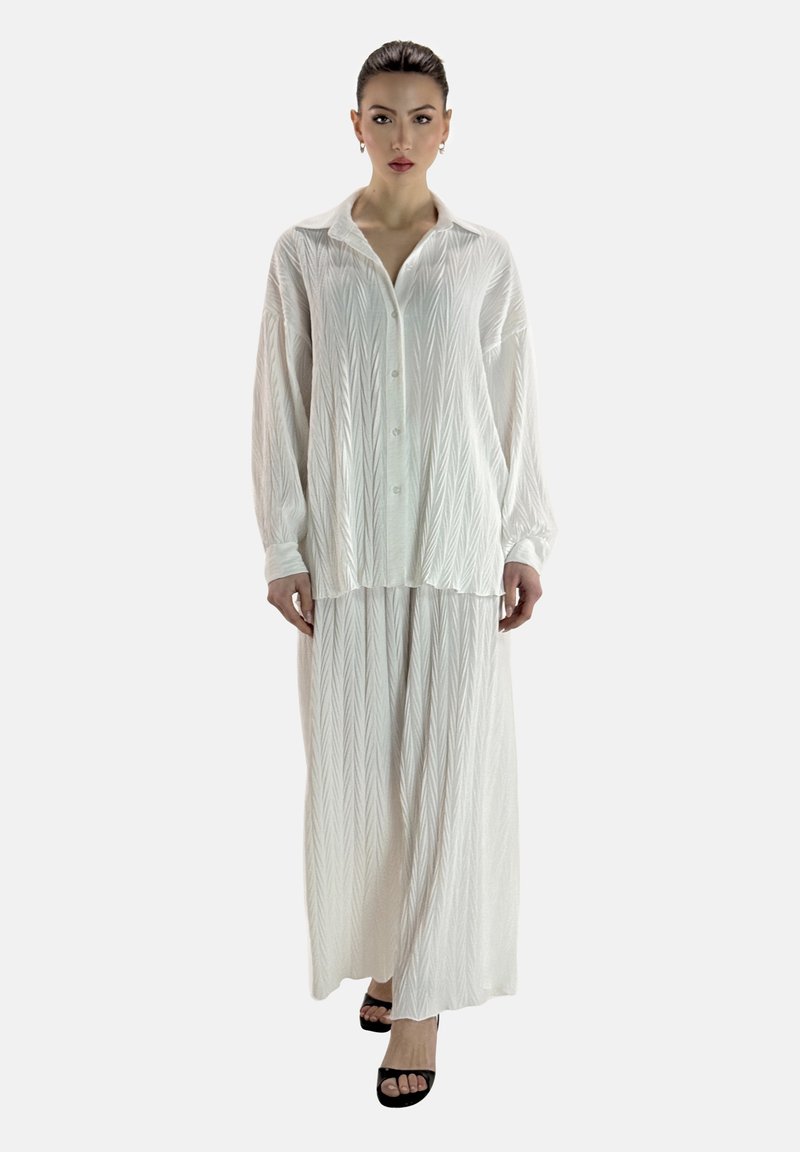 Chemise blanche à manches longues avec un devant boutonné et des rayures diagonales texturées, associée à une jupe longue assortie et des sandales à talons carrés noires.