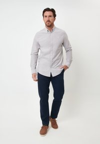 Camisa de botones gris claro de manga larga, combinada con pantalones azul marino oscuros y zapatos marrones. La camisa tiene cuello y un ajuste relajado.