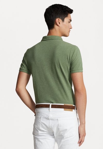 Camisa polo verde de manga corta con un acabado texturizado, que presenta un cuello y se combina con pantalones blancos y un cinturón marrón.