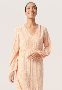 Långärmad klänning med V-ringning, tillverkad av lätt tyg, med ett mönster av orangea och vita blommor, samt detaljer med insamlad midja.