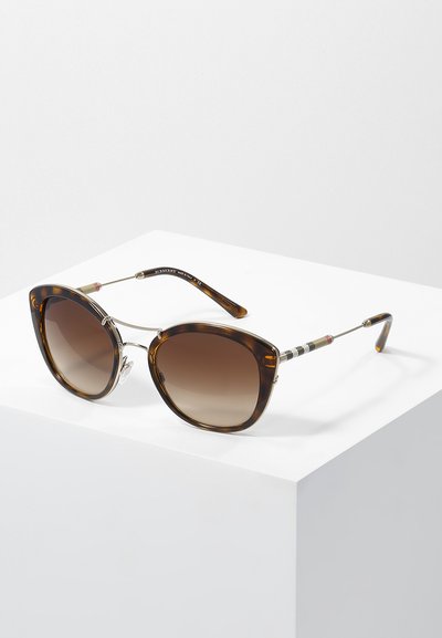 Ochelari de soare cu model tortoiseshell maroniu, cu formă de ochi de pisică, lentile cu degradé, brațe metalice subțiri și detalii stripe aproape de temple.