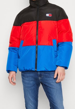 Homme portant une doudoune color block noire, rouge et bleue avec une fermeture éclair à l'avant et un logo Tommy Jeans sur la poitrine.