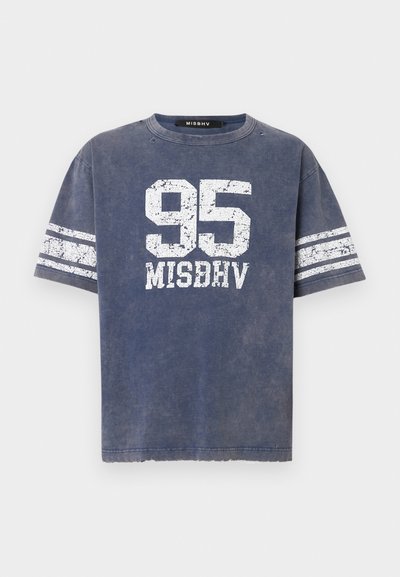 Zila kokvilnas T-kreklu ar apaļu kaklu, uz kura ir noberztas baltas "95" un "MISBHV" grafikas, kā arī baltas svītras uz piedurknēm.