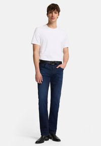 Hvid T-shirt med korte ærmer og mørkeblå denimjeans med bælte med en firkantet sort spænde og slim-fit pasform, båret med sorte læderstøvler.