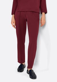 Pantalons bordeaux avec une texture lisse, coupe droite et coutures dessinées ; associés à des mocassins noirs à design tressé.