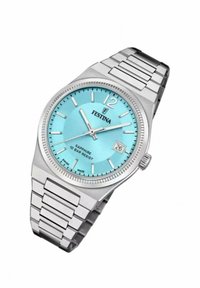 Reloj de acero inoxidable plateado con una esfera turquesa, marcadores de hora plateados y ventana para la fecha a las 6. Asegurado por una pulsera de metal enlazada.