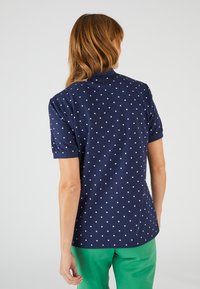 Polo navy con pois bianchi, maniche corte e colletto. Tessuto in misto cotone, texture liscia e vestibilità comoda.