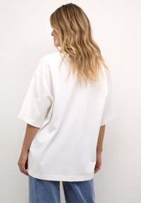 T-shirt bianca in cotone oversize con maniche corte e orlo dritto, abbinata a pantaloni in denim azzurro chiaro. Tessuto morbido, design minimal.