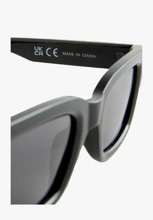 Mustad prillid, millel on matt viimistlus, ruudukujuline kuju ja tumedad läätsed. Sisemise varre peal on brändi logo. Valmistatud Hiinas.