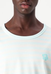 Light blue striped t-shirt featuring a floral design accent in a lighter shade. Soft fabric with a round neckline.