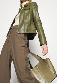 Veste en cuir vert olive avec fermeture éclair et détails à pressions, assortie à un pantalon ample marron et un sac fourre-tout texturé vert olive.