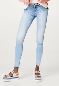 Vaaleansiniset kapeat farkut, jotka on valmistettu denimi-kankaasta ja joissa on sileä pinta sekä korkeavyötärö, yhdistetty hopeisiin korokepohjaisiin sandaaleihin.