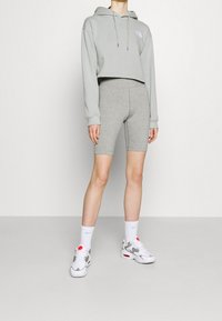 Sudadera corta de color gris claro con cordones y logo, combinada con pantalones cortos de ciclismo grises. Zapatillas blancas con detalles en rojo y gris.