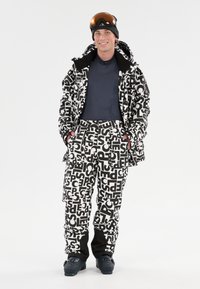 Zwart-witte skijas en -broek met gedurfde, grafische letters. De jas heeft een slim-fit ontwerp en de broek heeft cargozakken.