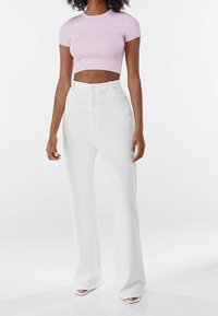 Svetle růžový růžkovaný krátký top spárovaný s bílými širokými kalhotami s vysokým pasem. Oblečení se vyznačuje hladkým povrchem a čistým, minimalistickým designem.