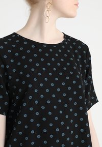 Haut noir à manches courtes avec un motif floral bleu, doté d'un col rond et d'une texture de tissu lisse et léger.