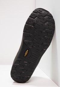 Black rubber shoe sole with a deep tread pattern, featuring the yellow "KEEN" logo. The design includes contours for traction and stability.