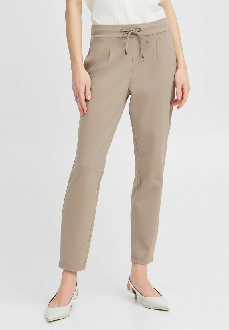 Beige Jogginghosen mit elastischem Bund und Kordelzug. Mit zwei Vordertaschen und schmalem Schnitt. Glattes Material mit matter Oberfläche.