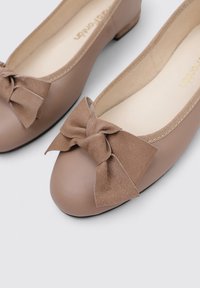 Bailarinas de cuero beige con punta redonda y un prominente lazo de ante en la parte delantera. El interior cuenta con un forro suave y una plantilla blanda.